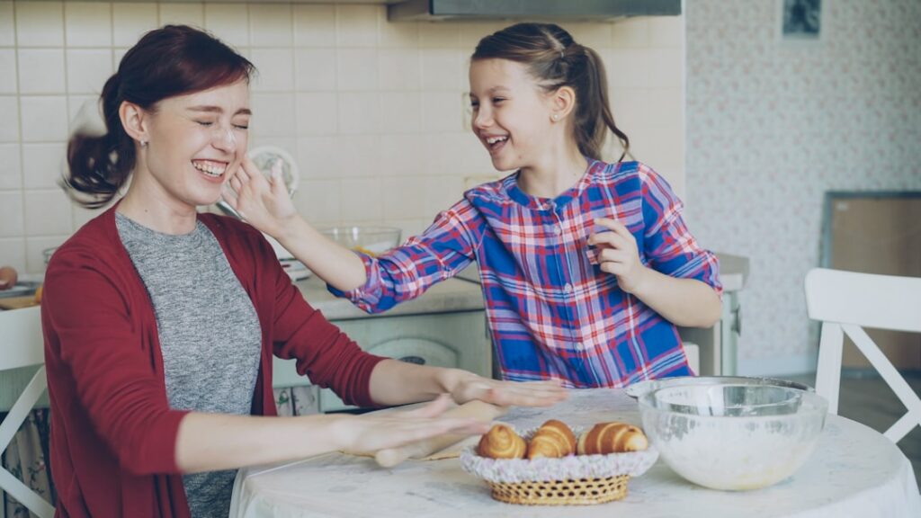 Woman with a joyful expression playfully dusting her hands with flour in a bright, sunlit kitchen, capturing the essence o...