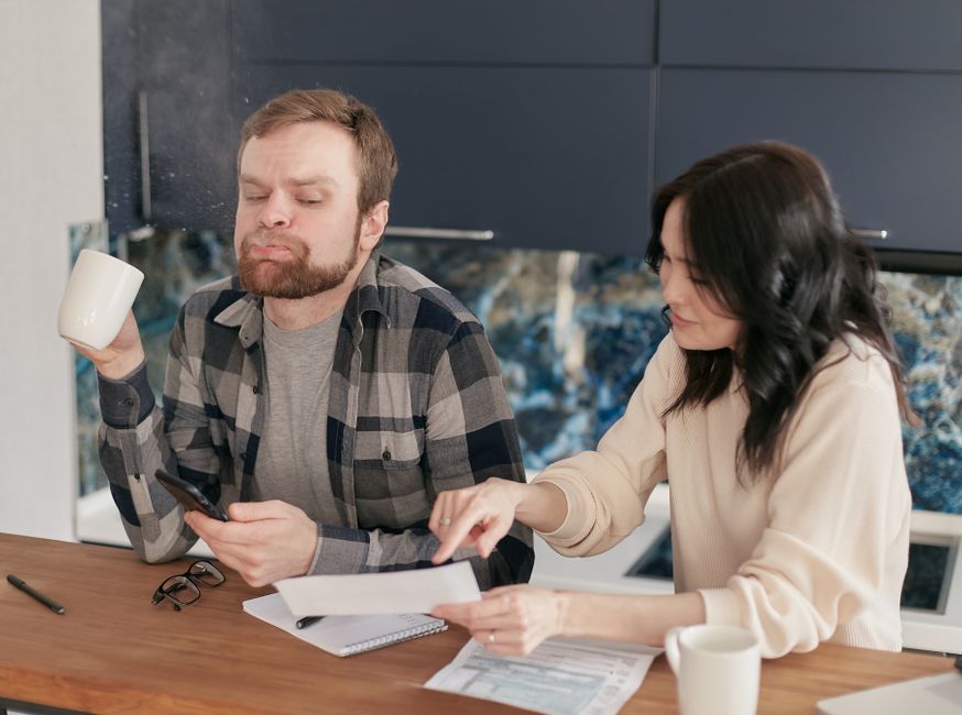 Smiling couple sits at a bright, modern kitchen island reviewing paperwork, symbolizing the financial relief and clarity f...